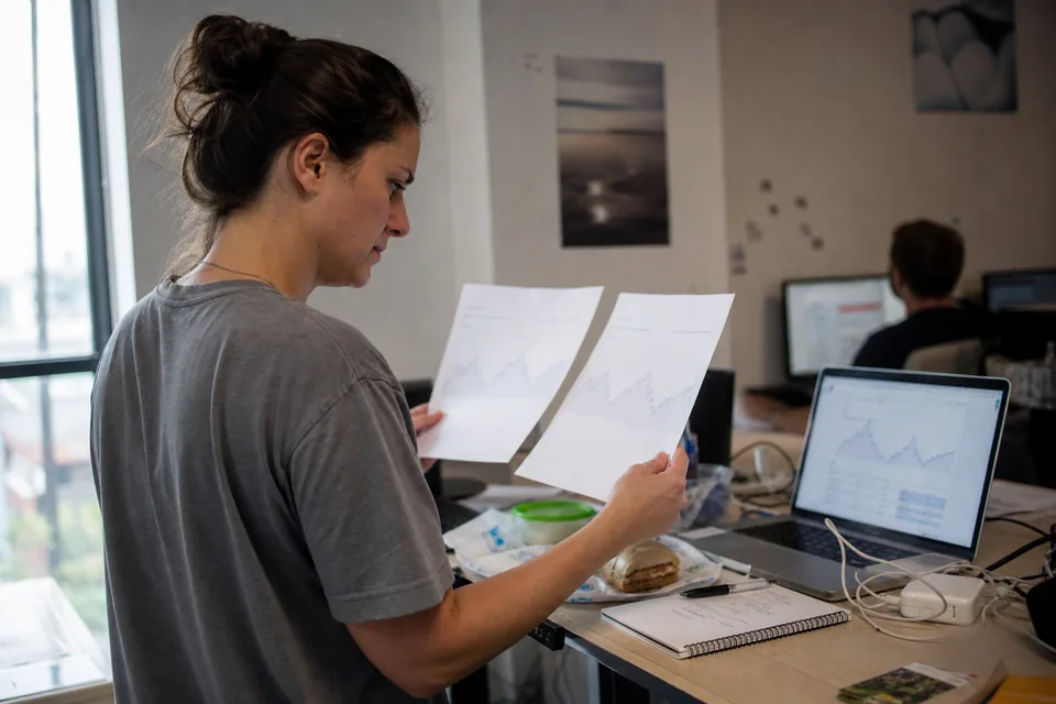 Developer at a standing desk weighing two API invoices next to a laptop with usage charts